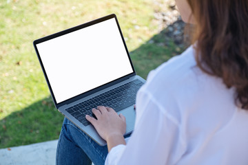 Mockup image of a woman using and typing on laptop with blank white screen , sitting in the outdoors with nature background