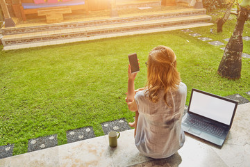 Freelancer girl with smartphone, coffee / tea and laptop on a home porch.
