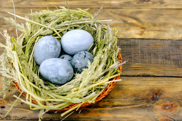 Easter eggs in green nest on wooden table.