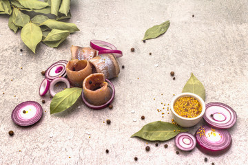 Rolled fillet of pickled Norwegian salted herring with spices and onions. Marinated fish on a stone background.