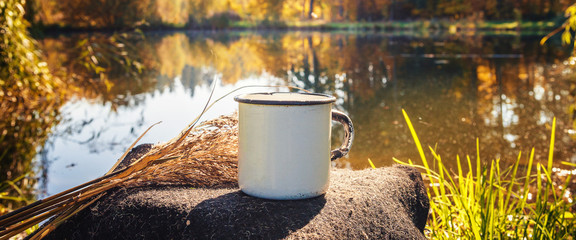 White cup with a drink on a stump near the lake, the idea of breakfast in travel tourism, a long banner