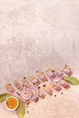 Pieces of pickled Norwegian salted herring with spices and onions. Marinated fish on a stone background, top view