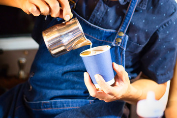 Aufgießen des Milchschaumes für einen Cappuccino im blauen Pappbecher