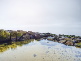 Fototapeta premium Stony coast defies to ocean clear sky with blurred Sun in high humidity.