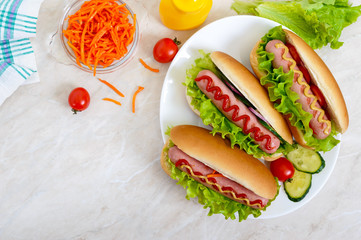 Tasty hot dogs with sausage grill, ketchup, mustard, lettuce, tomatoes on a white plate. The top view. Flat lay