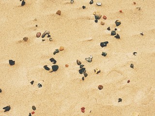 Sand of beach with soft waves and pebbles in sunny day