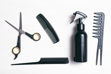 Hairdresser work table flatlay background. A various hairdressing tools such a hairbrushes, sprayer and a scissors on a white wooden board.