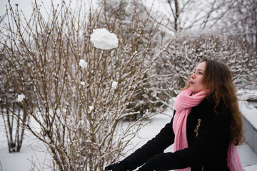 Young woman in coat throws up snow in winter