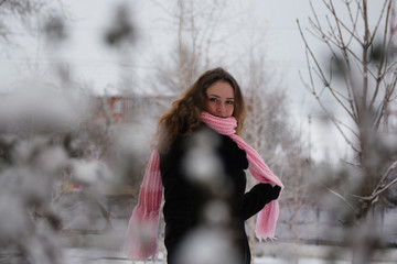 Young woman posing in a black coat and pink woolen scarf in the winter in the park