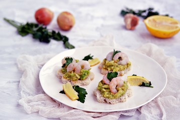 Small snack sandwiches on white bread with guacamole and shrimps on a white plate. Selective focus.