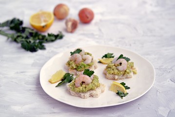 Small snack sandwiches on white bread with guacamole and shrimps on a white plate. Selective focus.