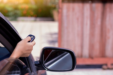 Woman in ca, hand pressing remote control to open or close the auto gate. Wireless technology...