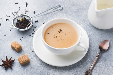 Cup of tea with milk, brown anise sugar on a grey table.
