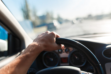 A man driving a car, focus on the left hand held on steering wheel