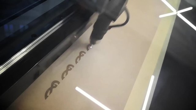 Color footage of a CNC laser machine engraving on wood.