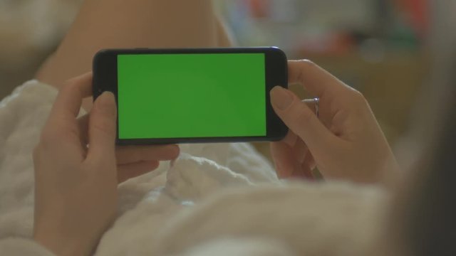 GREEN SCREEN Young Woman laying on a couch uses SmartPhone with pre-keyed green screen.