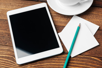 Digital tablet computer and cup of coffee on wooden desk.