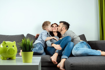 Happy parents and son having fun, tickling sitting together on the sofa, cheerful couple laughing,...