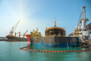 ships in dock yard under repairing with secured water pollution by safety guard rope floating...