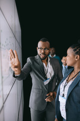 Black african businessman pointing and looking at large video screen for a presentation during a...