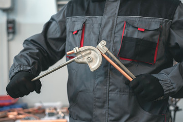 Pipe bender tool in a hands of factory worker on a factory workbench background. Fitter is bending...