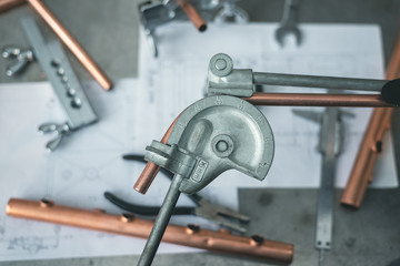 Pipe bender tool in a hands of factory worker on a factory workbench background. Fitter is bending a pipe. Pipework.