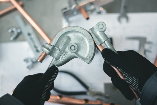 Pipe bender tool in a hands of factory worker on a factory workbench background. Fitter is bending a pipe. Pipework.