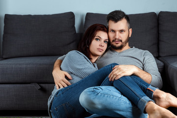 Obraz premium Portrait of a beautiful young couple looking at the camera, against a gray sofa.