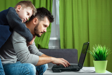 Father and son working on a laptop. Businessman working from home and looking after a child, spending time with a child. The concept of StartUp, Freelance, a successful modern family.