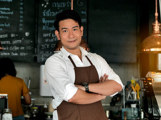 Happy Asian barista crossed arm in front of bar, lifestyle concept.