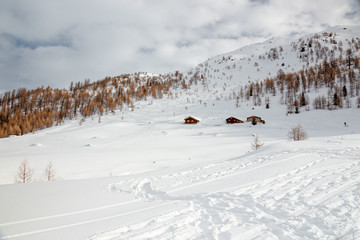 panoramic view of a mountain pasture with huts submerged by the snow on a sunny winter day.