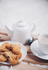 Cozy breakfast in bed, cup of coffee and heart shaped waffles on wooden tray on white and gray cozy blanket, the concept of home comfort, copy space