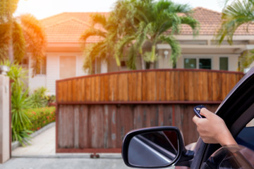  Woman in car, hand using remote control to open the automatic gate with modern home...