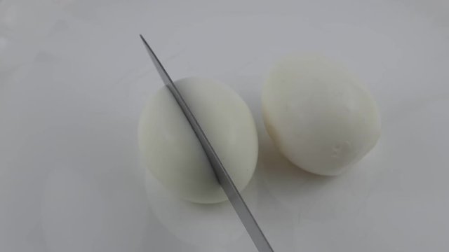 Boiled eggs are cut with a knife into two halves on a white plate