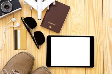 Digital tablet with empty white screen, passport accessories and plane model mock up on wooden background.