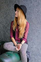 Girl Hipster in a black bowler hat and a Burgundy shirt sitting on a leather green sofa and looking...