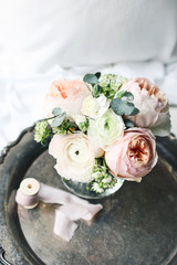 Cozy bedroom still life scene. Wedding, birthday bouquet of pink English roses, Ranunculus and Astrantia flowers and silk ribbon on vintage silver tray.Feminine styled composition. Top view, defocused