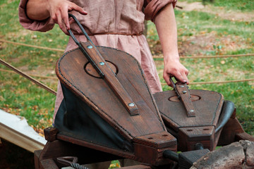 Blacksmith in ancient clothes squeezing bellows to kindle fire in furnace. Reconstruction