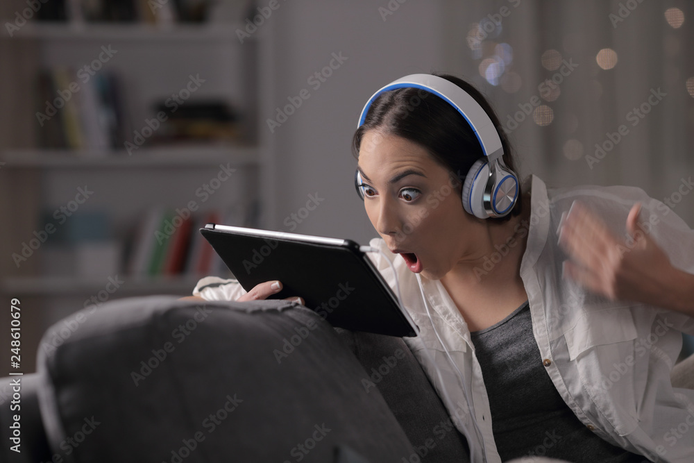 Wall mural Surprised girl with headphones checks tablet content