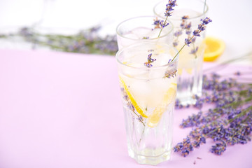 Lavender lemonade with lemon and ice on purple background.