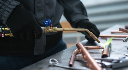 Worker is soldering a pipe by a blow lamp on a factory workbench background. Pipework.