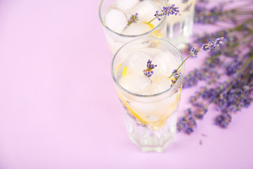 Lavender lemonade with lemon and ice on purple background.