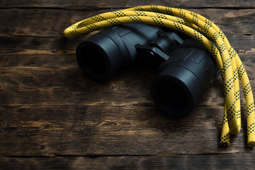 Safety rope and binoculars on a brown wooden board background with copy space.