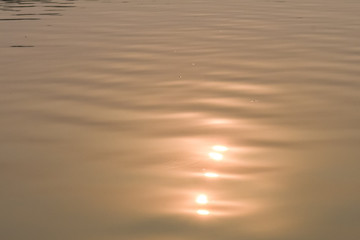 Beautiful sunset water background. Soft wave of the sea. At twilight times and reflections. Golden and orange colors in the waves. Abstract creative background.