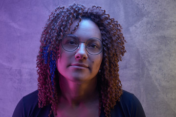 Portrait of an authentic adult woman with afro curls against a black wall in the studio. Unusual...
