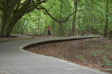 Beautiful caucasian female running down a winding  wooden path in the forest in summer sunshine