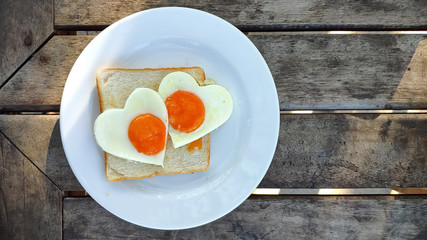 Breakfast for Valentines day with love. Fried eggs in the shape of a heart at toast on white plate and wooden table on the beach