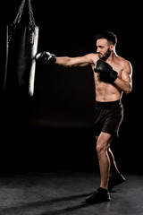 bearded athlete wearing boxing gloves hitting punching bag on black background