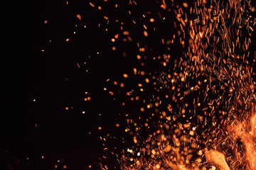 Burning sparks flying. Beautiful flames. Fiery orange glowing flying away particles on black...