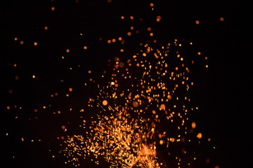 Burning sparks flying. Beautiful flames. Fiery orange glowing flying away particles on black...